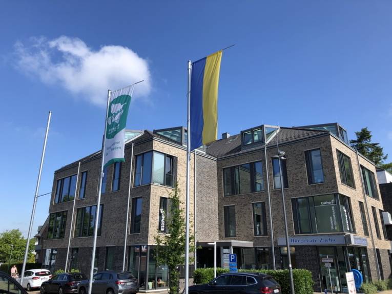 Die grün-weiße-Mayors-for-Peace-Flagge weht neben einer Flagge in den ukrainischen Nationalfarben vor einem Gebäude in Halstenbek (Schleswig-Holstein) im Wind.